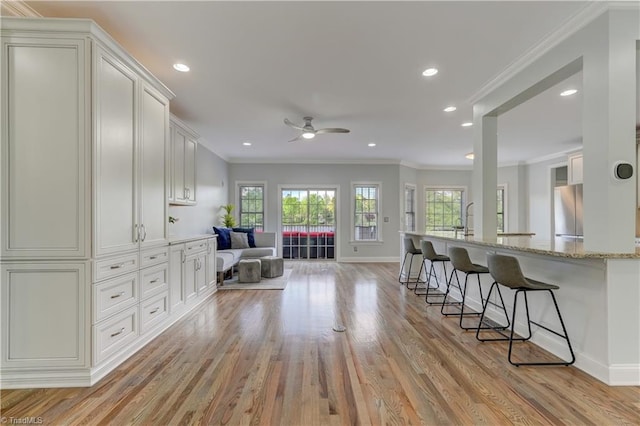 kitchen with stainless steel fridge, ornamental molding, a ceiling fan, a kitchen breakfast bar, and light stone countertops