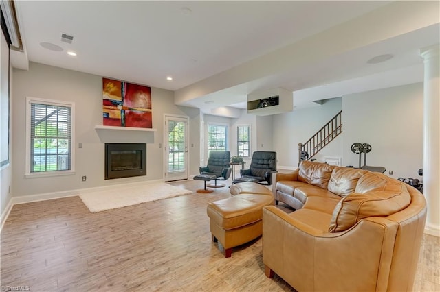 living room featuring light wood-type flooring, a glass covered fireplace, plenty of natural light, and stairs