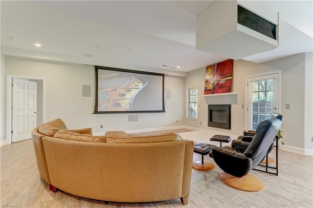 home theater with recessed lighting, baseboards, light wood finished floors, and a glass covered fireplace