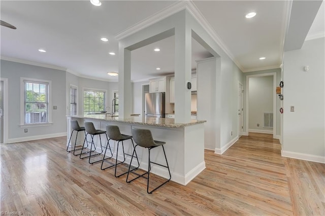 kitchen featuring light wood-type flooring, a breakfast bar, white cabinetry, freestanding refrigerator, and visible vents