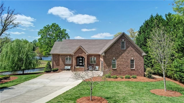 view of front of house featuring brick siding, a front yard, a water view, and driveway