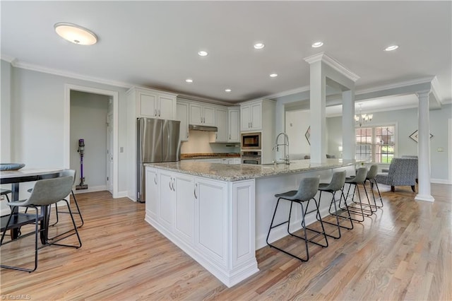 kitchen with light wood-style floors, appliances with stainless steel finishes, a kitchen bar, and light stone countertops