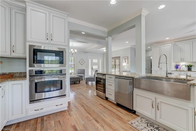 kitchen with appliances with stainless steel finishes, ornamental molding, light wood-style floors, wine cooler, and a sink