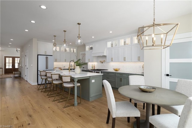 kitchen with freestanding refrigerator, custom range hood, backsplash, a kitchen island with sink, and recessed lighting