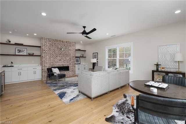 living area featuring a ceiling fan, light wood finished floors, recessed lighting, and a brick fireplace