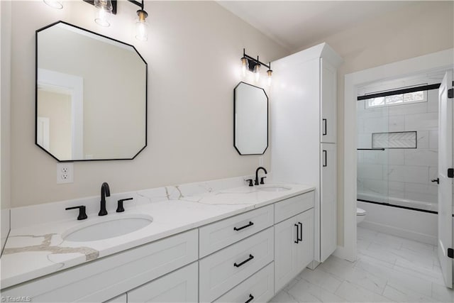 bathroom featuring marble look tile flooring, double vanity, toilet, and enclosed tub / shower combo