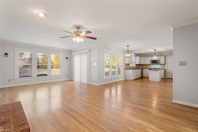 unfurnished living room featuring crown molding, sink, ceiling fan with notable chandelier, and light hardwood / wood-style flooring