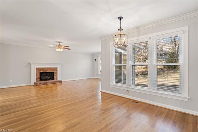 unfurnished living room featuring ornamental molding, a fireplace, ceiling fan with notable chandelier, and light wood-type flooring