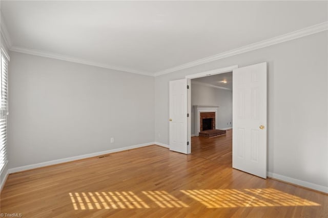 empty room featuring crown molding, a brick fireplace, and hardwood / wood-style flooring