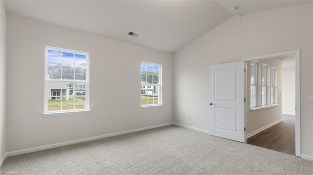 spare room with lofted ceiling, a healthy amount of sunlight, and dark colored carpet