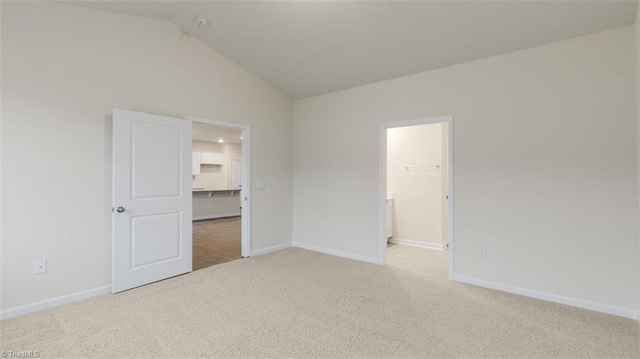 unfurnished bedroom featuring a walk in closet, a closet, vaulted ceiling, and carpet flooring