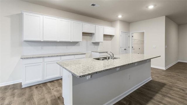 kitchen with a kitchen island with sink, light stone countertops, sink, and white cabinetry