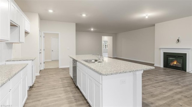 kitchen with an island with sink, dishwasher, light stone countertops, white cabinets, and sink