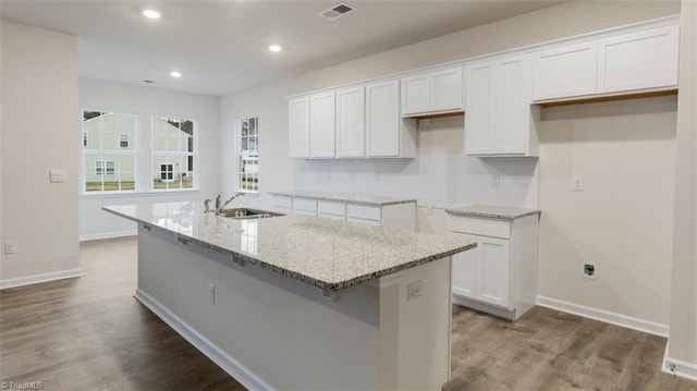 kitchen featuring light stone countertops, white cabinetry, and a kitchen island with sink