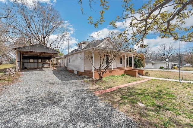 view of front of house featuring a detached carport, a front yard, gravel driveway, and an outbuilding