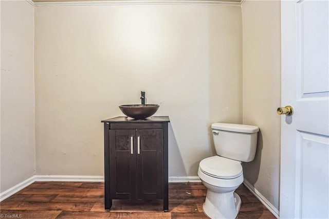 half bath featuring toilet, vanity, baseboards, and wood finished floors