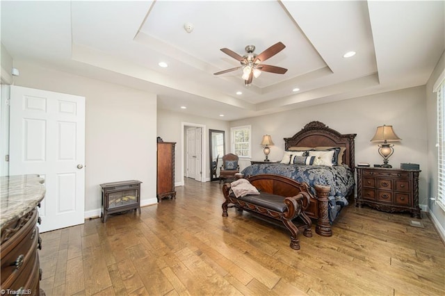 bedroom with a tray ceiling, a wood stove, wood-type flooring, baseboards, and recessed lighting