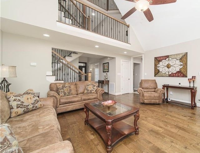 living area with high vaulted ceiling, stairs, a ceiling fan, wood finished floors, and baseboards