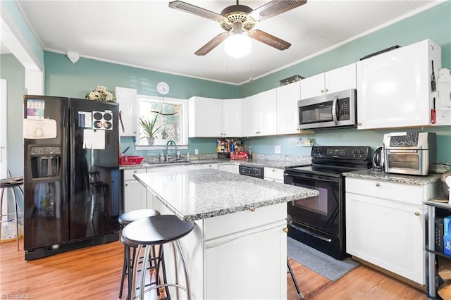 kitchen featuring a breakfast bar, black appliances, light wood-type flooring, and a sink