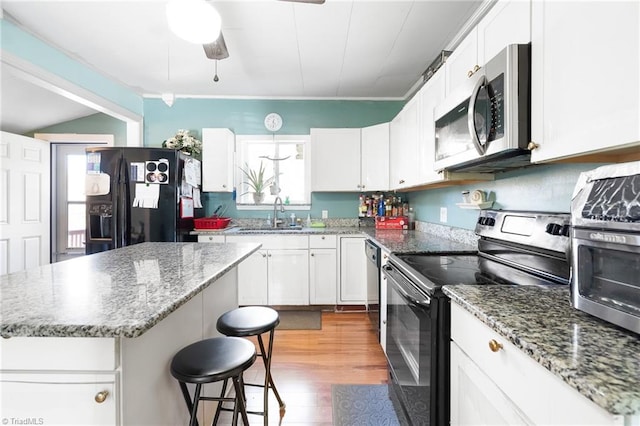 kitchen featuring a kitchen bar, black appliances, a sink, white cabinets, and ceiling fan