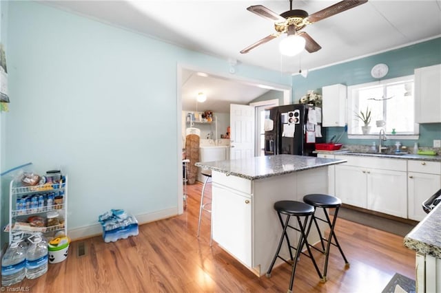 kitchen featuring a sink, a kitchen island, wood finished floors, a breakfast bar area, and black refrigerator with ice dispenser