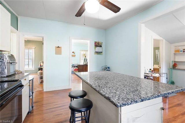 kitchen with light wood finished floors, a center island, ceiling fan, a breakfast bar, and white cabinets