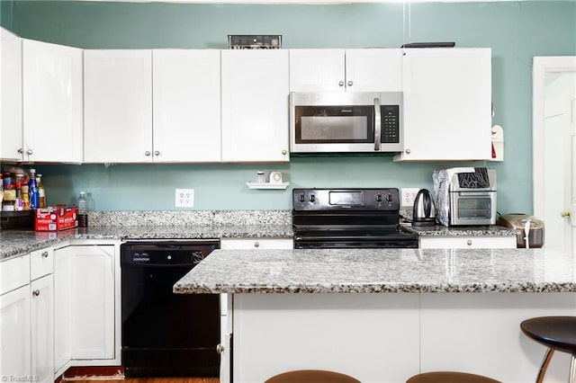 kitchen with a kitchen breakfast bar, black appliances, white cabinets, and light stone countertops