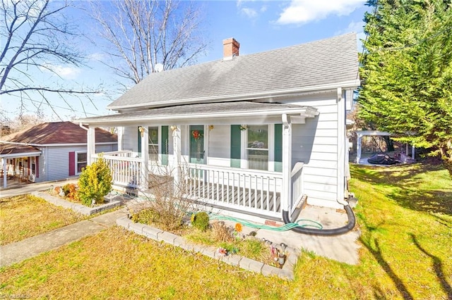 bungalow-style house with a porch, a chimney, a front yard, and roof with shingles