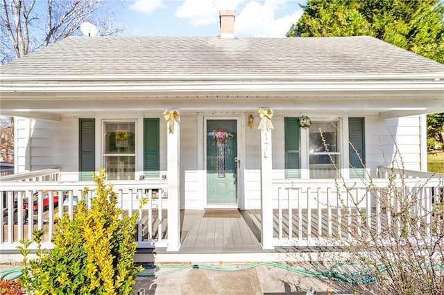 view of front of house featuring a chimney, a porch, and a shingled roof