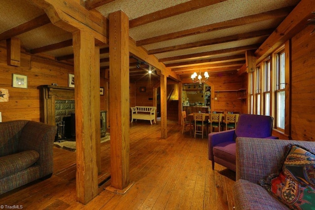 living room with wood walls, beamed ceiling, a notable chandelier, wood-type flooring, and a fireplace