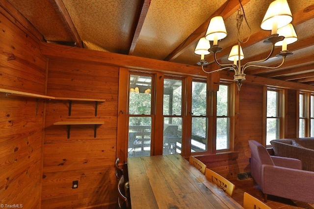 dining area featuring an inviting chandelier, wood walls, a wealth of natural light, and beamed ceiling