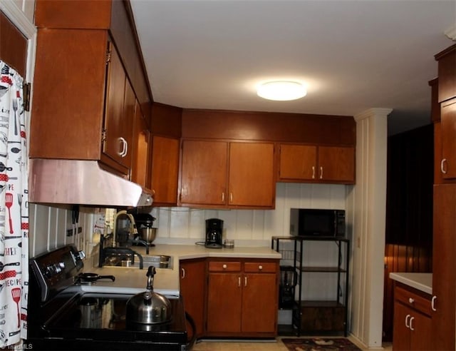 kitchen featuring brown cabinetry, range hood, light countertops, black appliances, and a sink