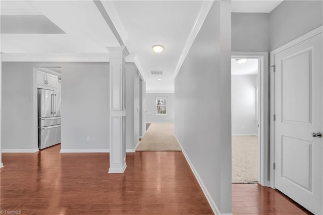 corridor with dark wood-type flooring, visible vents, baseboards, ornate columns, and crown molding