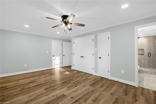 unfurnished bedroom featuring ensuite bathroom, wood-type flooring, ornamental molding, ceiling fan, and multiple closets