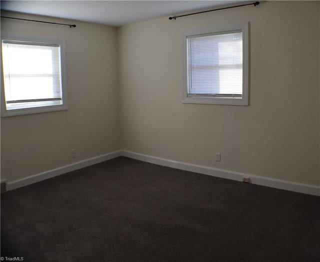 spare room featuring dark carpet and baseboards