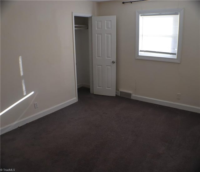 unfurnished bedroom featuring visible vents, baseboards, a closet, and dark carpet