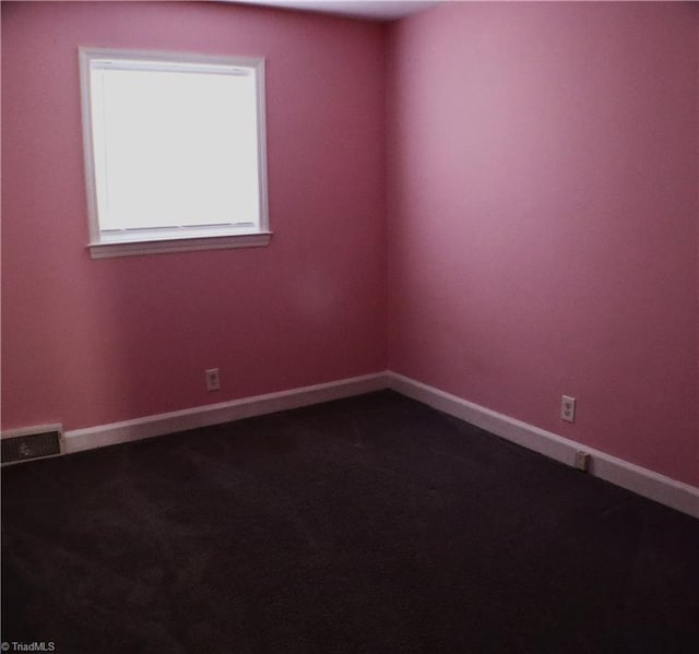 spare room featuring visible vents, dark colored carpet, and baseboards