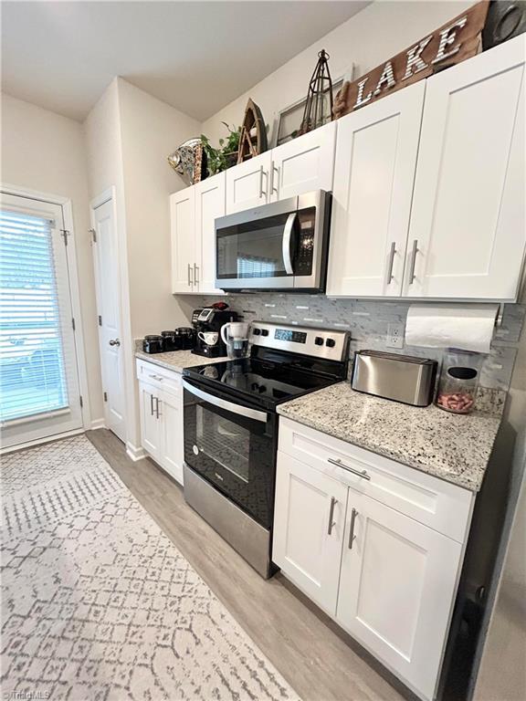 kitchen featuring light hardwood / wood-style flooring, appliances with stainless steel finishes, light stone counters, white cabinets, and decorative backsplash