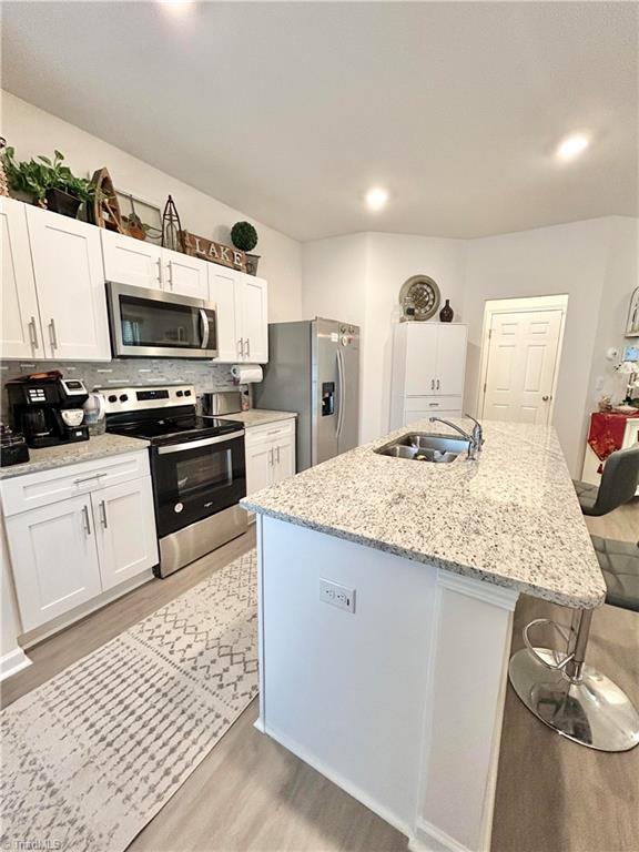 kitchen with white cabinetry, stainless steel appliances, and a center island with sink