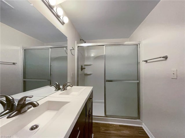 full bathroom featuring double vanity, a stall shower, a sink, and wood finished floors