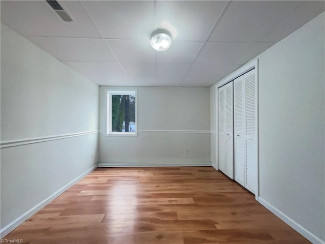 unfurnished bedroom featuring baseboards, visible vents, a drop ceiling, and wood finished floors