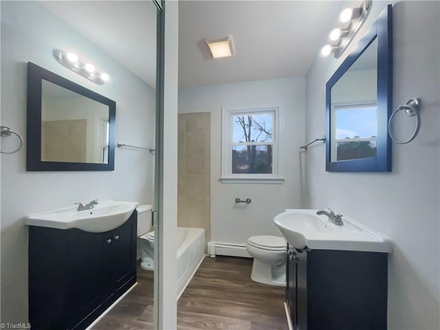 full bathroom featuring two vanities, toilet, baseboard heating, and wood finished floors