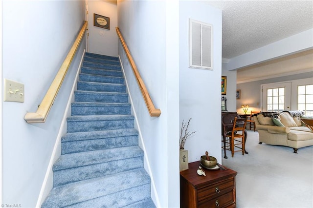 stairway with carpet flooring and a textured ceiling