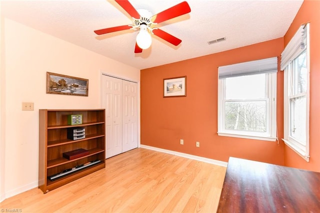 unfurnished bedroom featuring ceiling fan, a textured ceiling, light hardwood / wood-style floors, and a closet