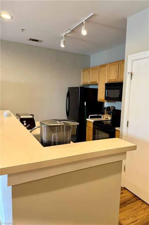 411 Washington St Unit 204, Greensboro, NC 27401 - kitchen featuring black appliances, track lighting, light countertops, light brown cabinetry, and light wood-type flooring