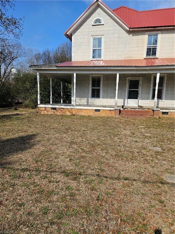 farmhouse-style home with metal roof, covered porch, and a front yard