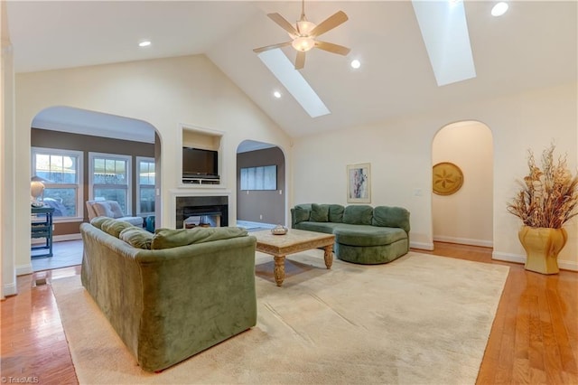 living room with a skylight, high vaulted ceiling, ceiling fan, and light hardwood / wood-style flooring