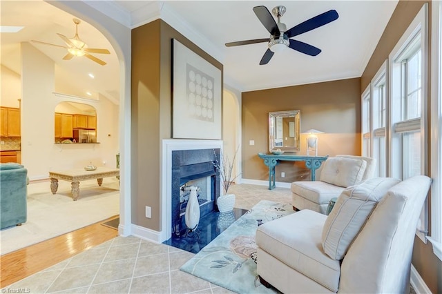 living area with ceiling fan, a tiled fireplace, ornamental molding, and light hardwood / wood-style flooring