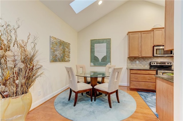 dining space featuring high vaulted ceiling, a skylight, and light hardwood / wood-style floors