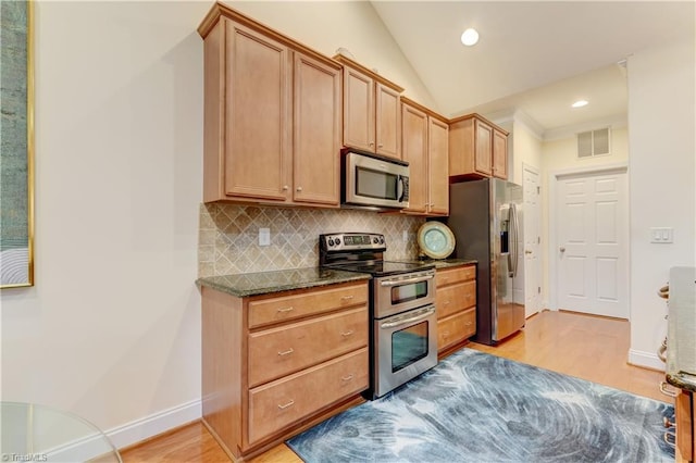 kitchen with stainless steel appliances, lofted ceiling, light wood-type flooring, backsplash, and dark stone countertops